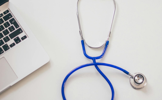 A blue stethoscope is placed next to the keyboard of an open laptop on a white surface.