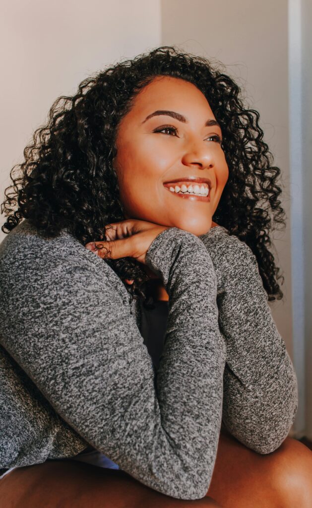 Smiling woman resting her chin on her hands, looking relaxed and hopeful.