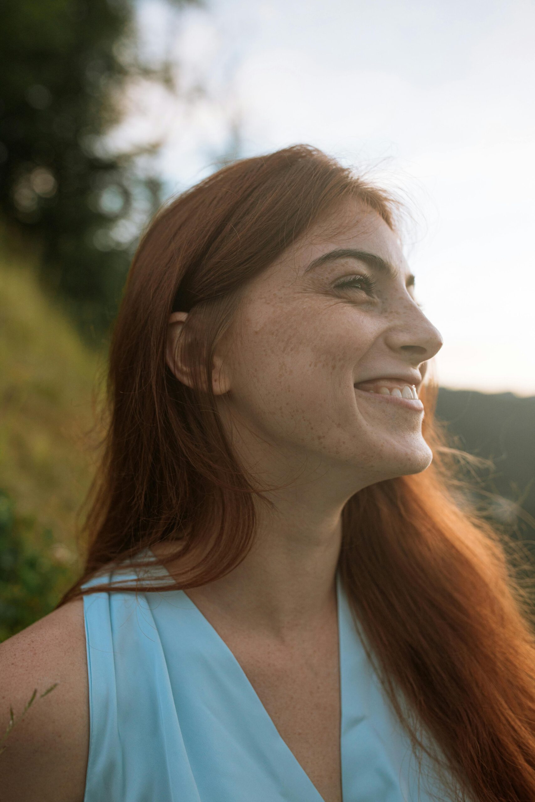A woman with red hair smiles joyfully in warm golden sunlight outdoors, conveying the vitality, confidence, and renewed well-being that personalized care at Abundant Health & Wellness makes possible